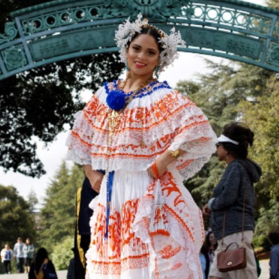 A young woman in traditional Latina dress stands under an arch
