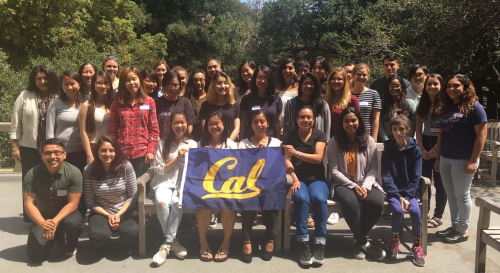 A large group of mostly female students posing for a photo holding a Cal banner on an outside patio at UC Berkeley.