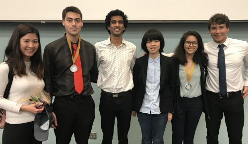 Six students, two who are each wearing an award medallion, stand shoulder to shoulder in front of a projection screen, pose for a photo together.
