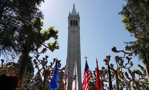 An upward view of UC Berkeley's clock tower with flags staged at the bottom.