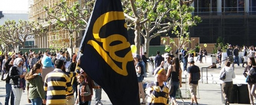 Group of students walking through Sproul Plaza carrying a large Cal flag.