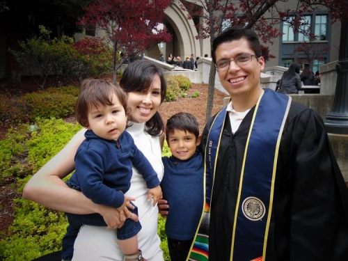 Individual in graduation gown and stole emblazoned with Berkeley logo stands with three family members outside of a building.