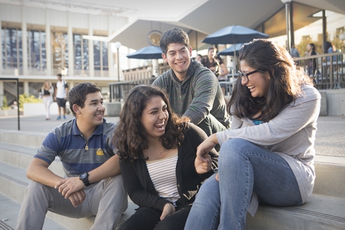 Two female and two male students sitting down on steps outside a building share a laugh together.