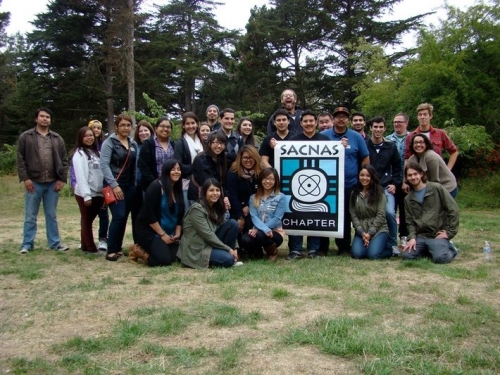 Large group of students posing for a photo holding a SACNAS chapter banner outdoors.