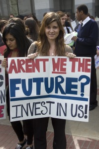 A student holds a sign reading "Aren't We the Future? Invest in Us!"