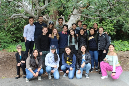 A group of scholars pose in front of a large tree.