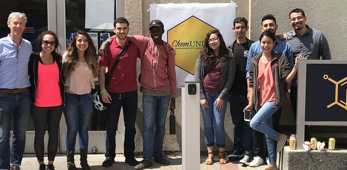 A group of ten chemUNITY members standing outside smiling for a photo in front of their organization logo