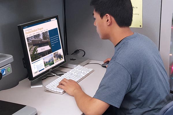 A young man sitting a computer viewing the Disabled Students Program webpage
